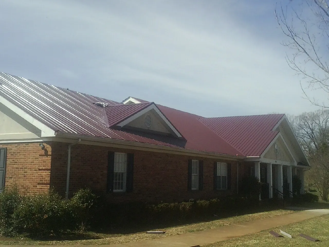 Red metal roof with gabled entries on a long brick building, from a Hail Damage Roof Repair job in Weldon
