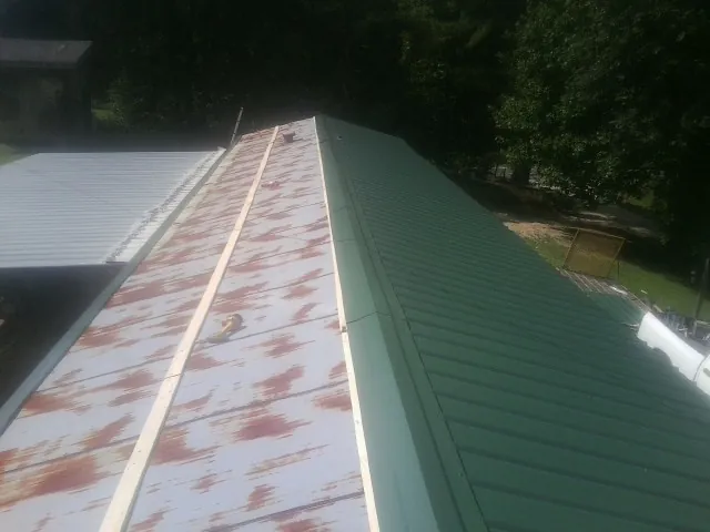Old rusted panels beside newly installed green metal roofing — Wind Damage Roof Repair by Roofing Brothers in Weldon