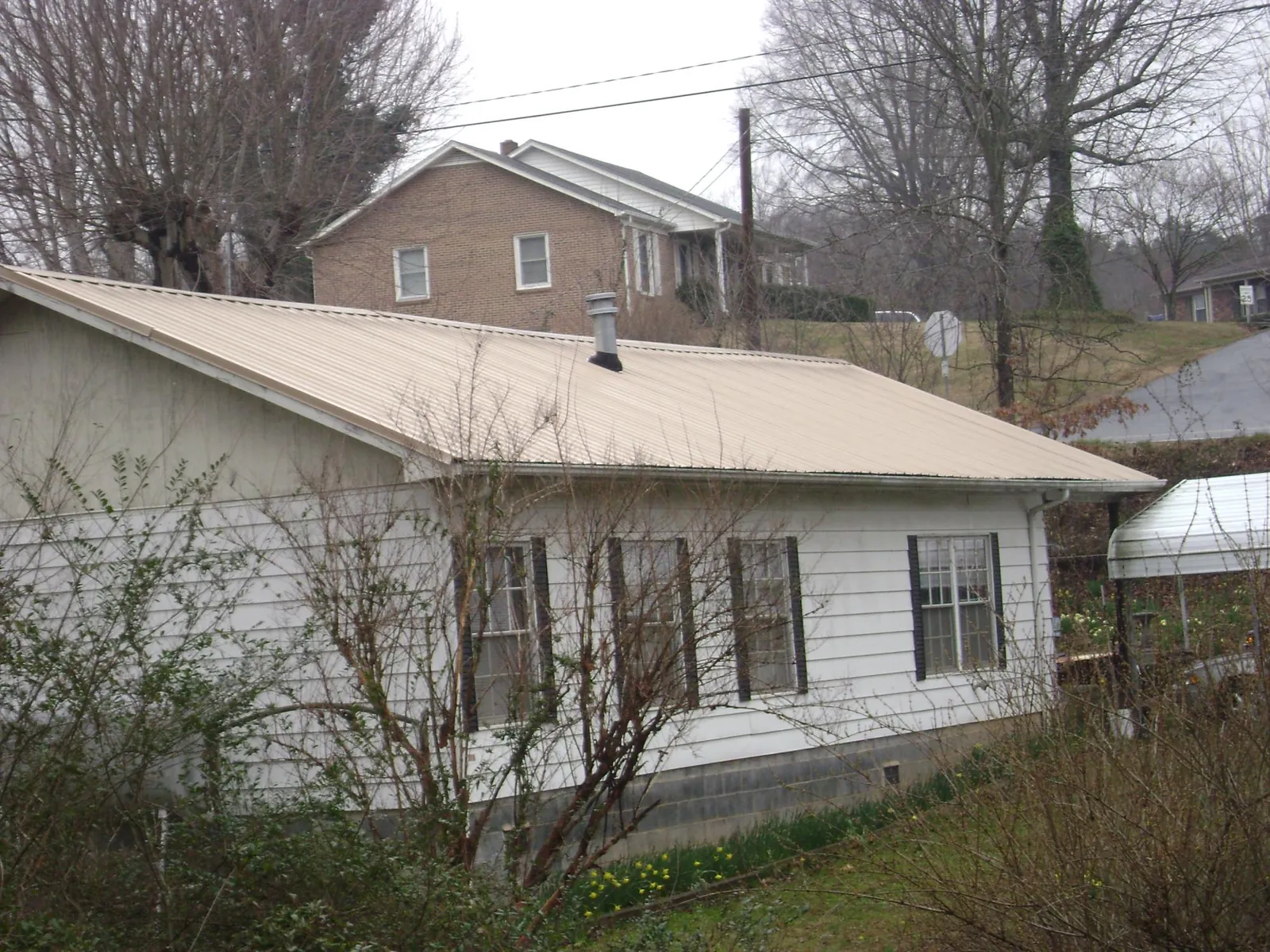 Tan metal roof on a white sided house set into a hillside — Commercial Roofing by Roofing Brothers in Weldon