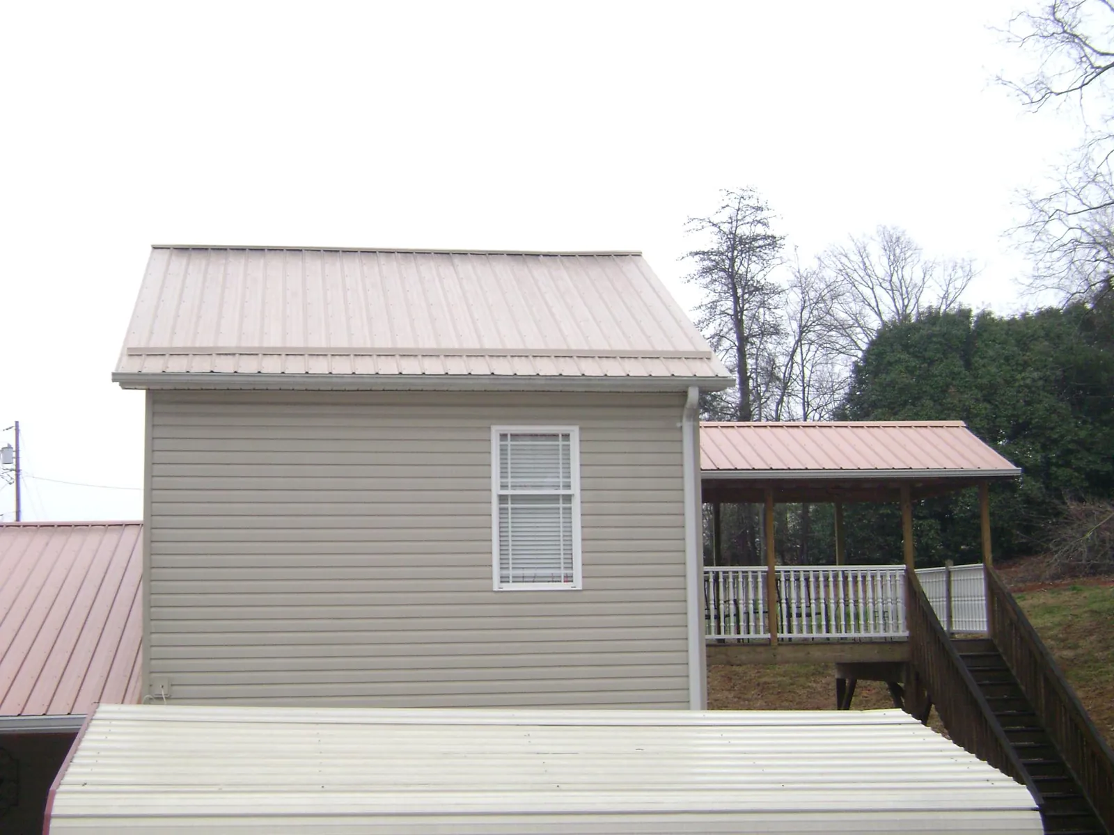 Tan metal roofs on a two story addition and attached porch, from a Roof Replacement job in Weldon